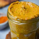 A jar of tom yum paste on a table next to a bowl of spices.