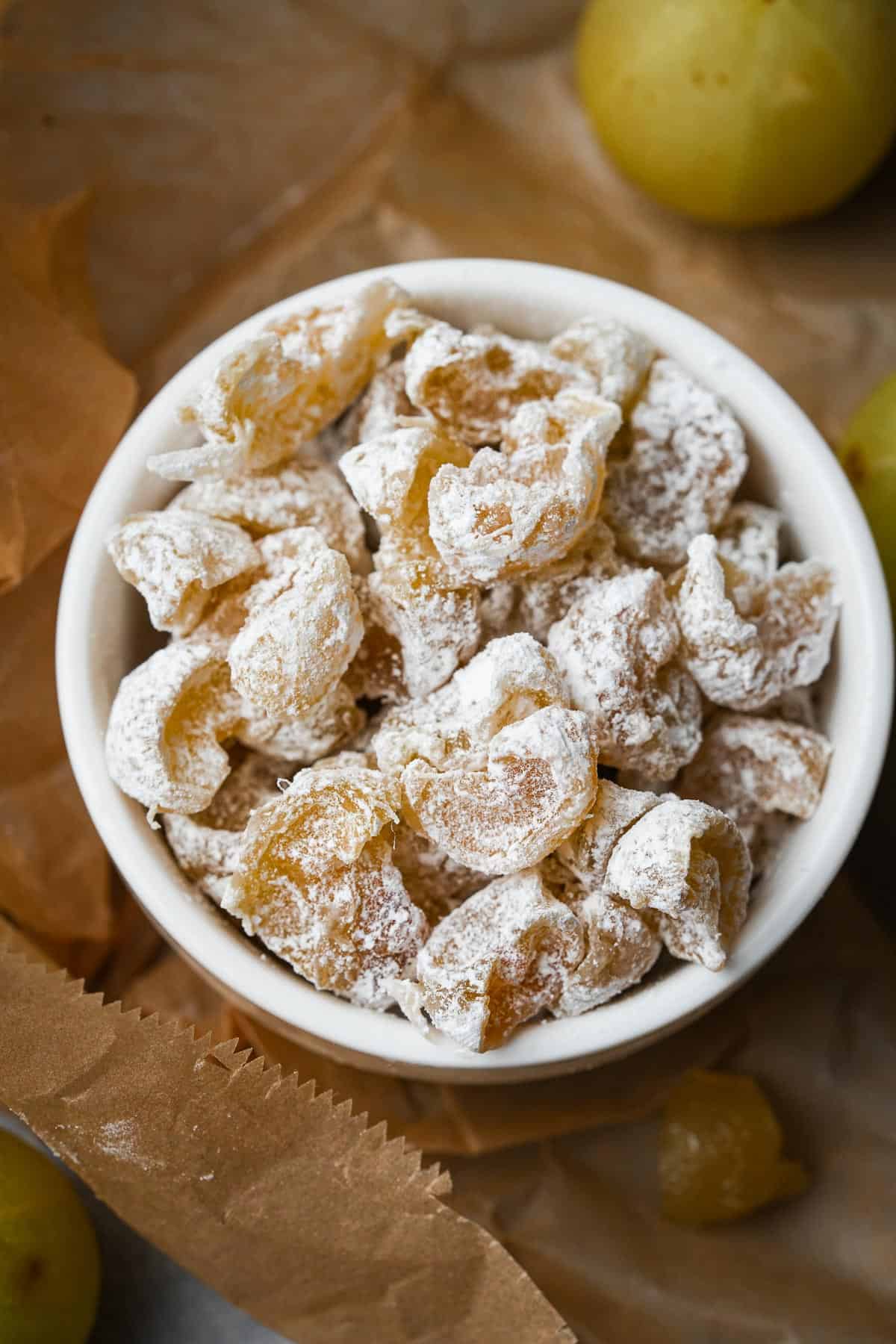 A bowl of powdered sugar-coated amla candy sitting on top of a piece of brown paper.