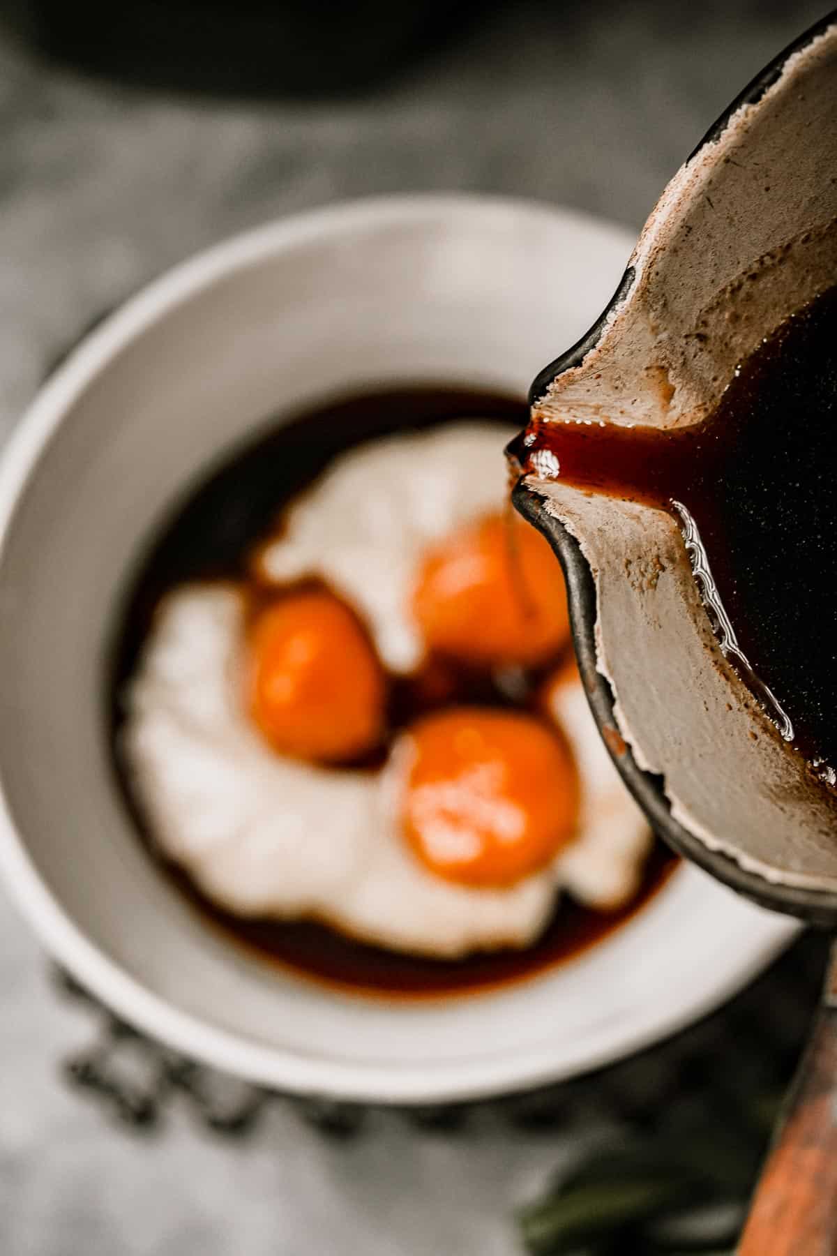 Palm sugar syrup being poured into a bowl of buber sum sum with biji salak dumplings in it.