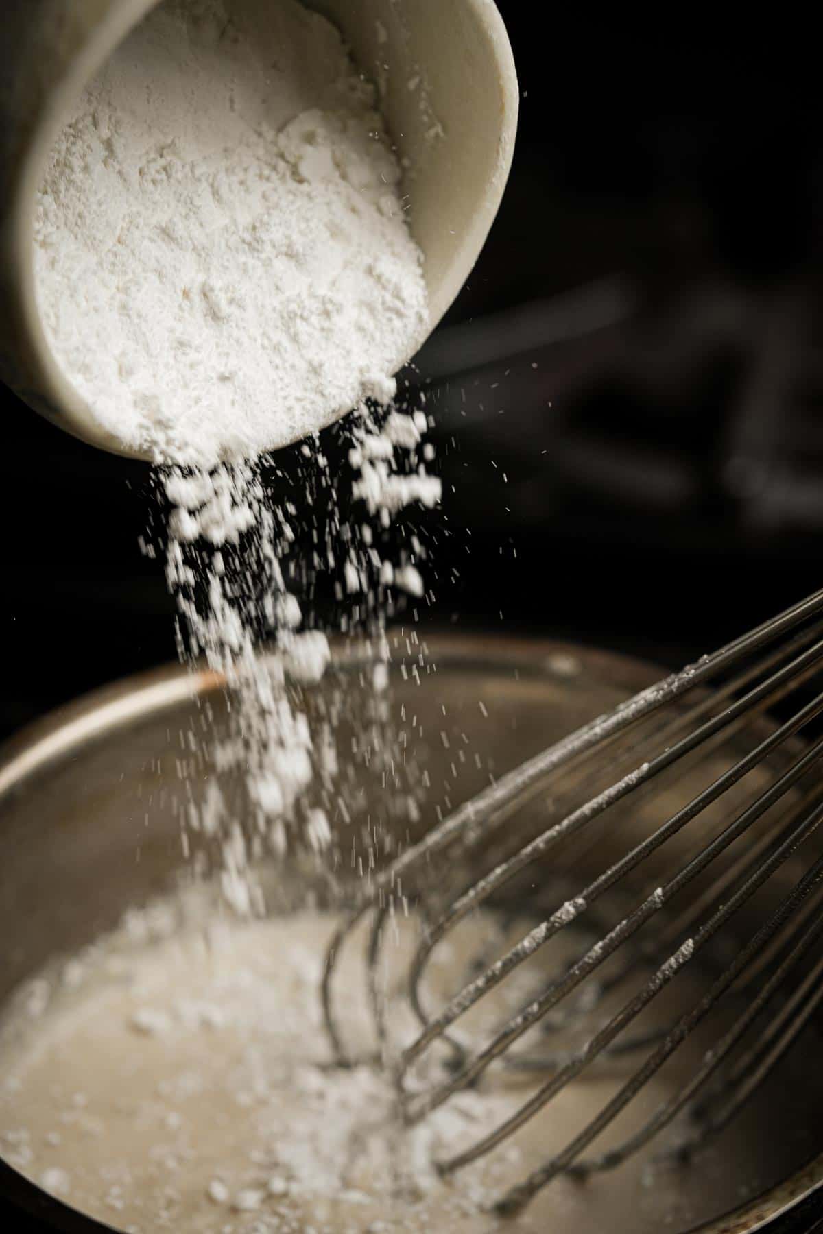 Sweet rice flour being poured into a pan with a whisk.