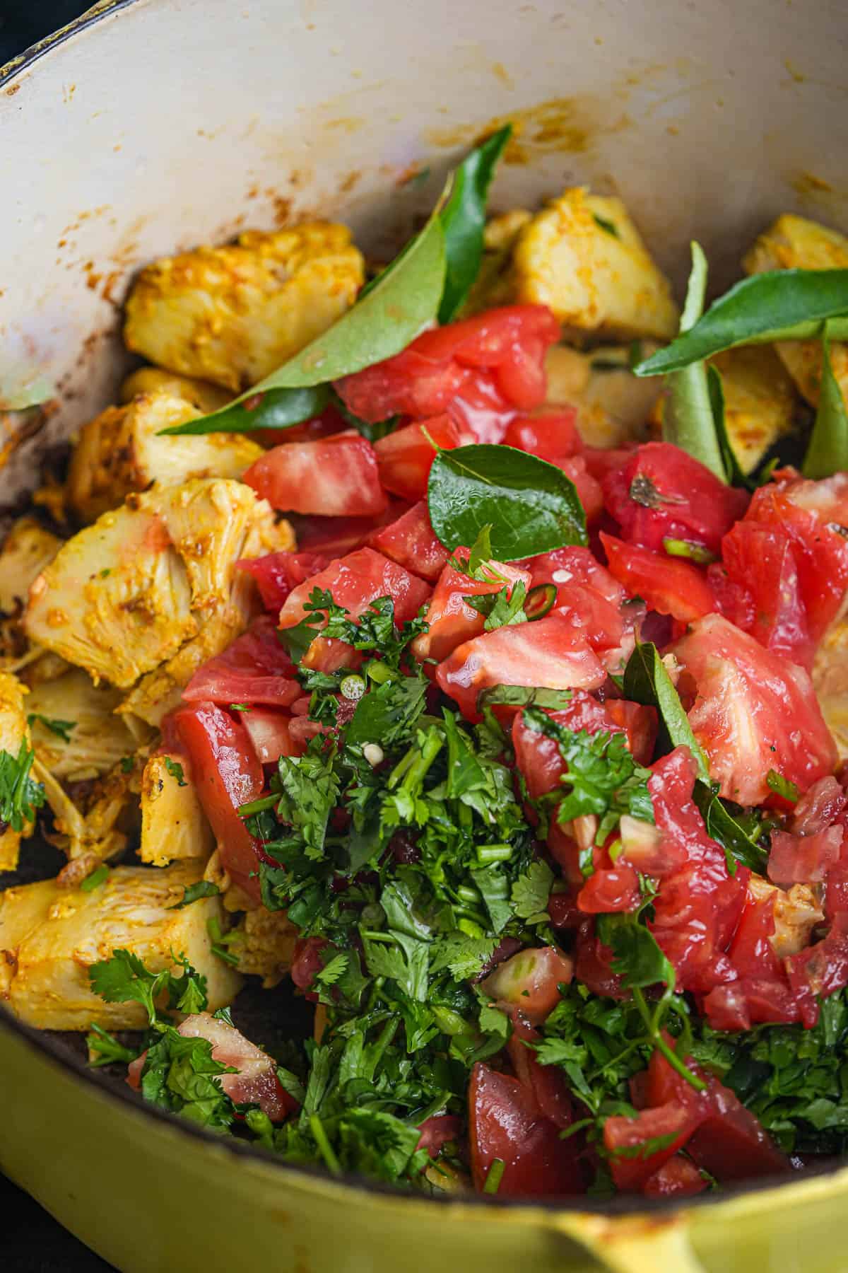 herbs and tomatoes are added to the pot of cooking jackfruit.