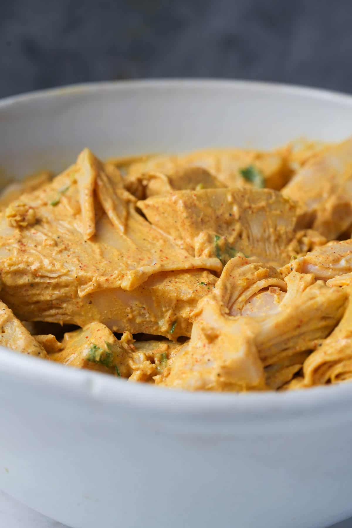 A white bowl filled with jackfruit marinating in a spicy yogurt sauce.
