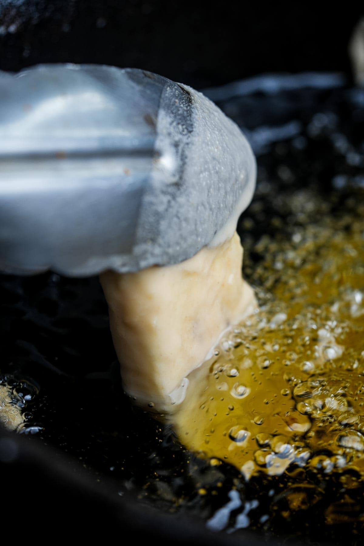 A frying pan with a piece of batter coated banana being dipped into it.