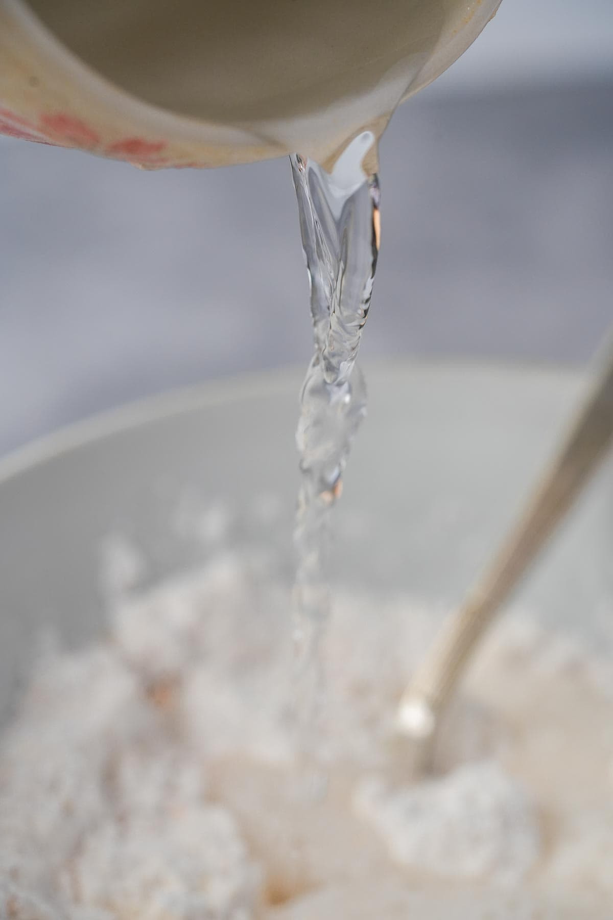 Ice cold water is being poured into a bowl of flour.