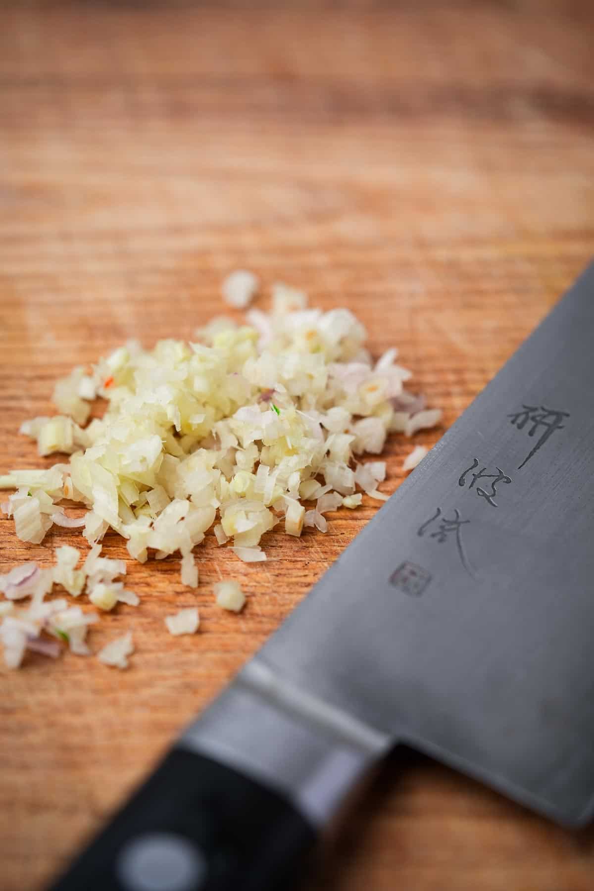 A knife with chopped lemongrass on top of a wooden cutting board.