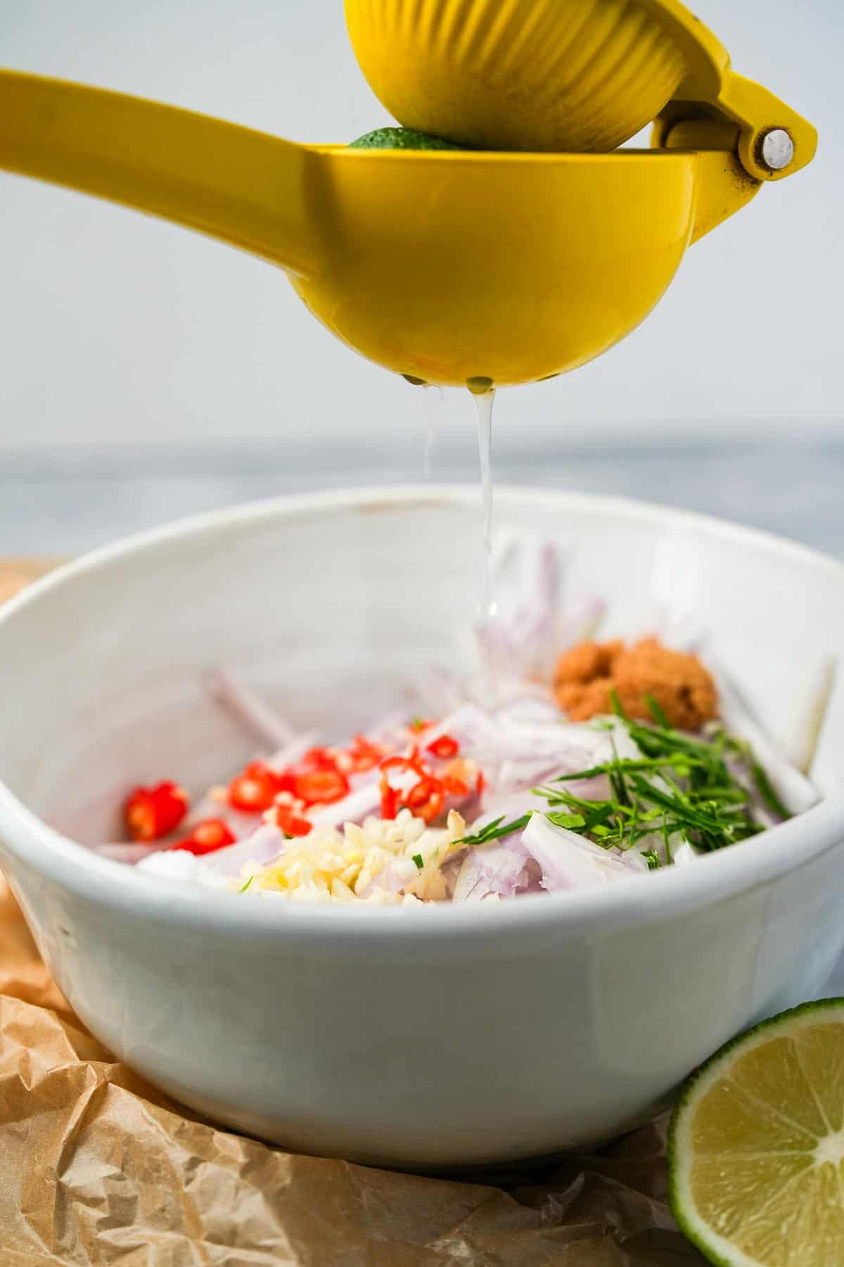 A lime is being freshly juiced into a bowl of shallots and chilies.