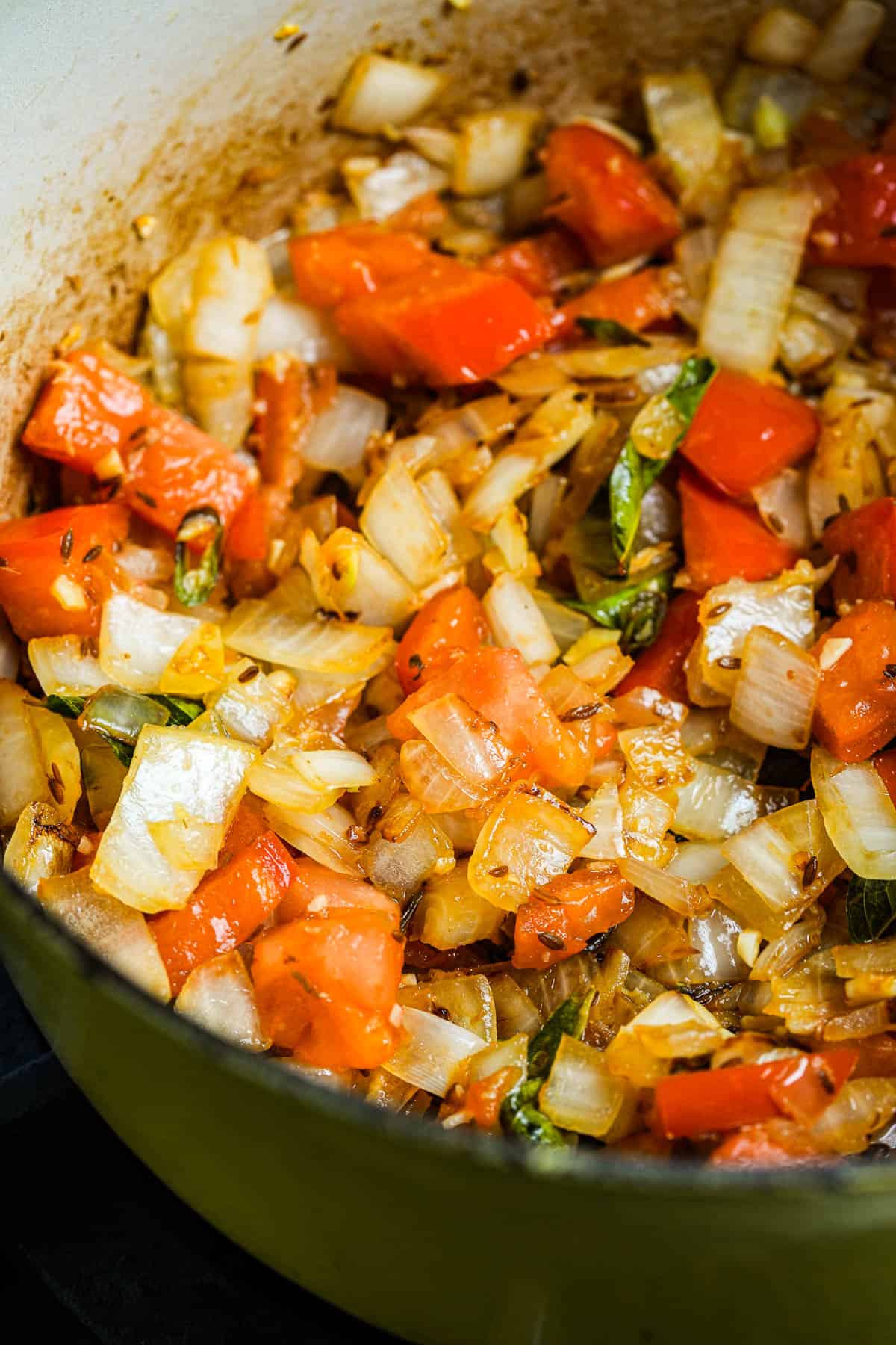 A pan with onions, tomatoes, and seasonings cooking in it.