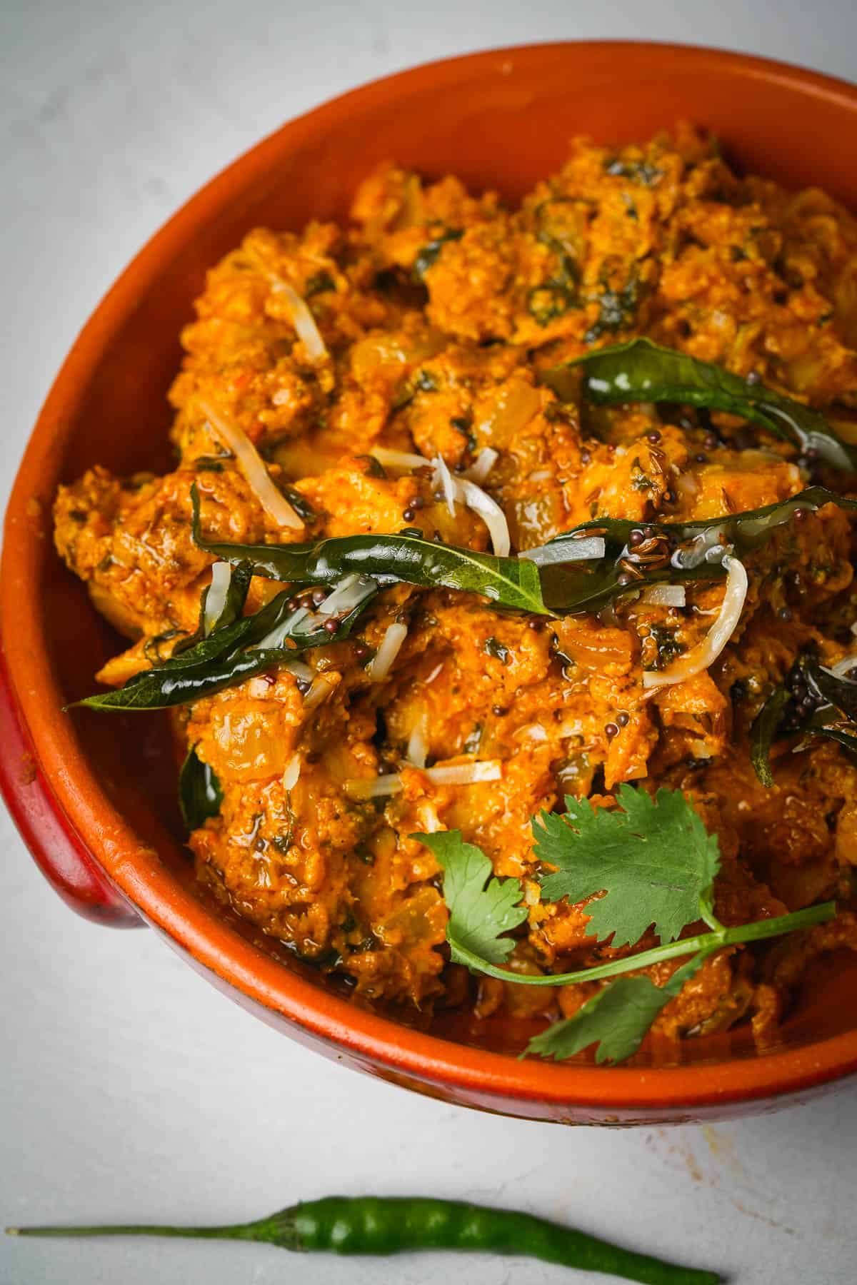 An orange bowl of soya chaap curry on a table.
