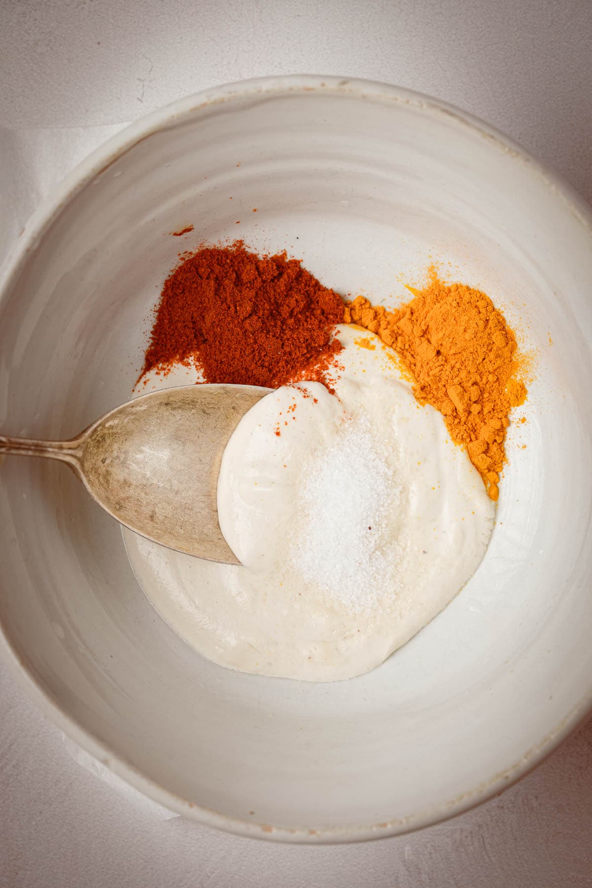 A white bowl with a spoon mixing up vegan yogurt with spices and salt.
