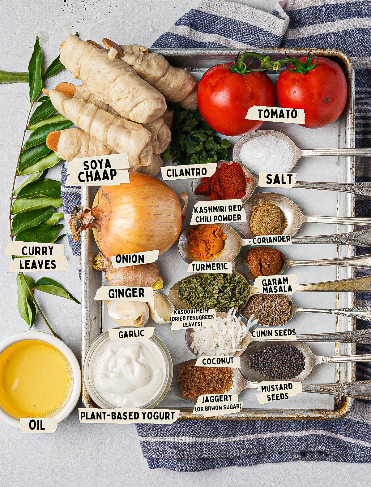 A beautifully arranged tray brimming with assorted spices and ingredients like tomatoes, ginger, and aromatic curry leaves. The treasures of cumin seeds, turmeric, coriander, and soya chaap are neatly labeled.