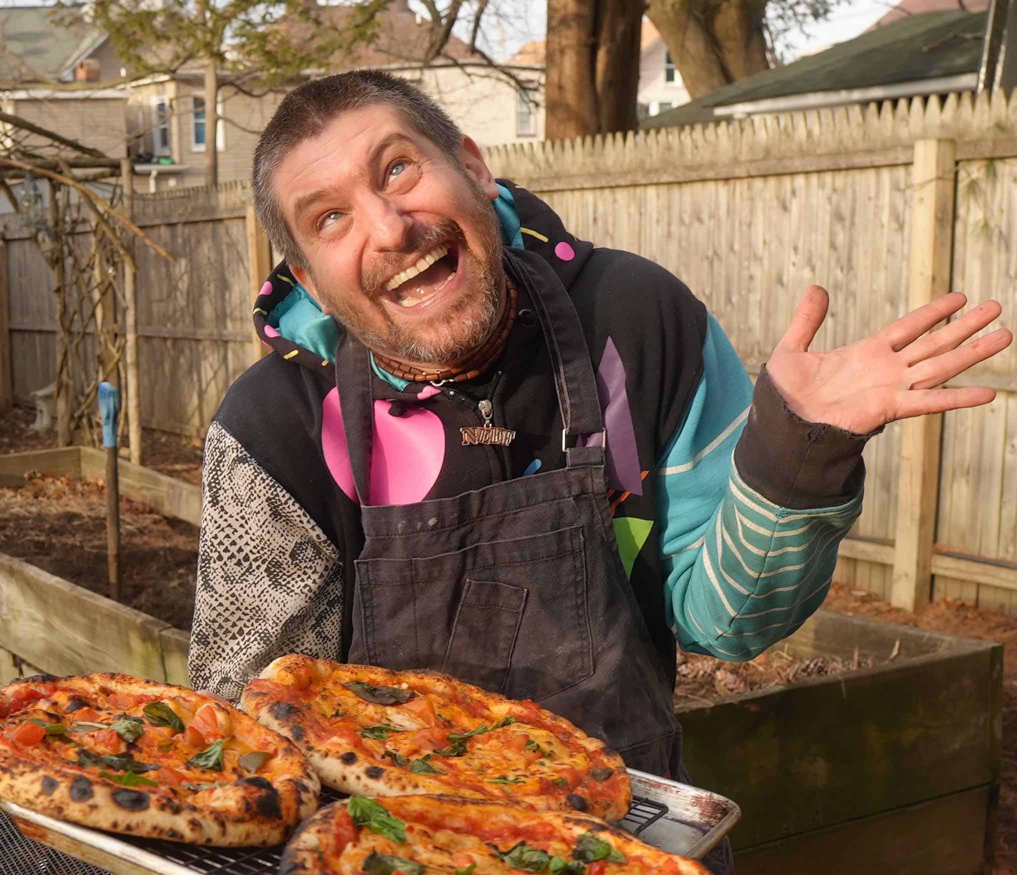 Chef Adam Sobel laughing while holding fresh vegan pizzas