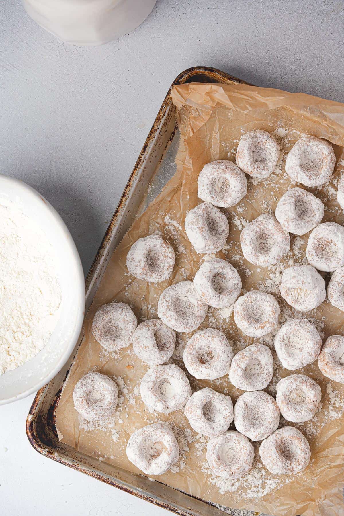 A tray of fellah koftesi, formed and coated in flour on a table next to a bowl of flour.