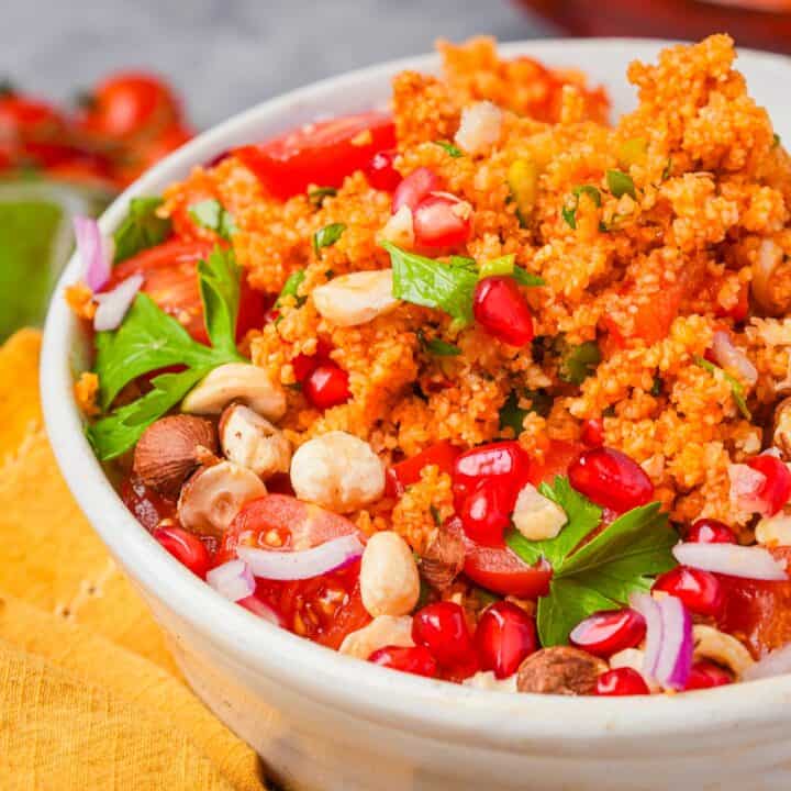 A bowl of kisir bulgur salad with tomatoes, herbs, pomegranate seeds, and nuts.