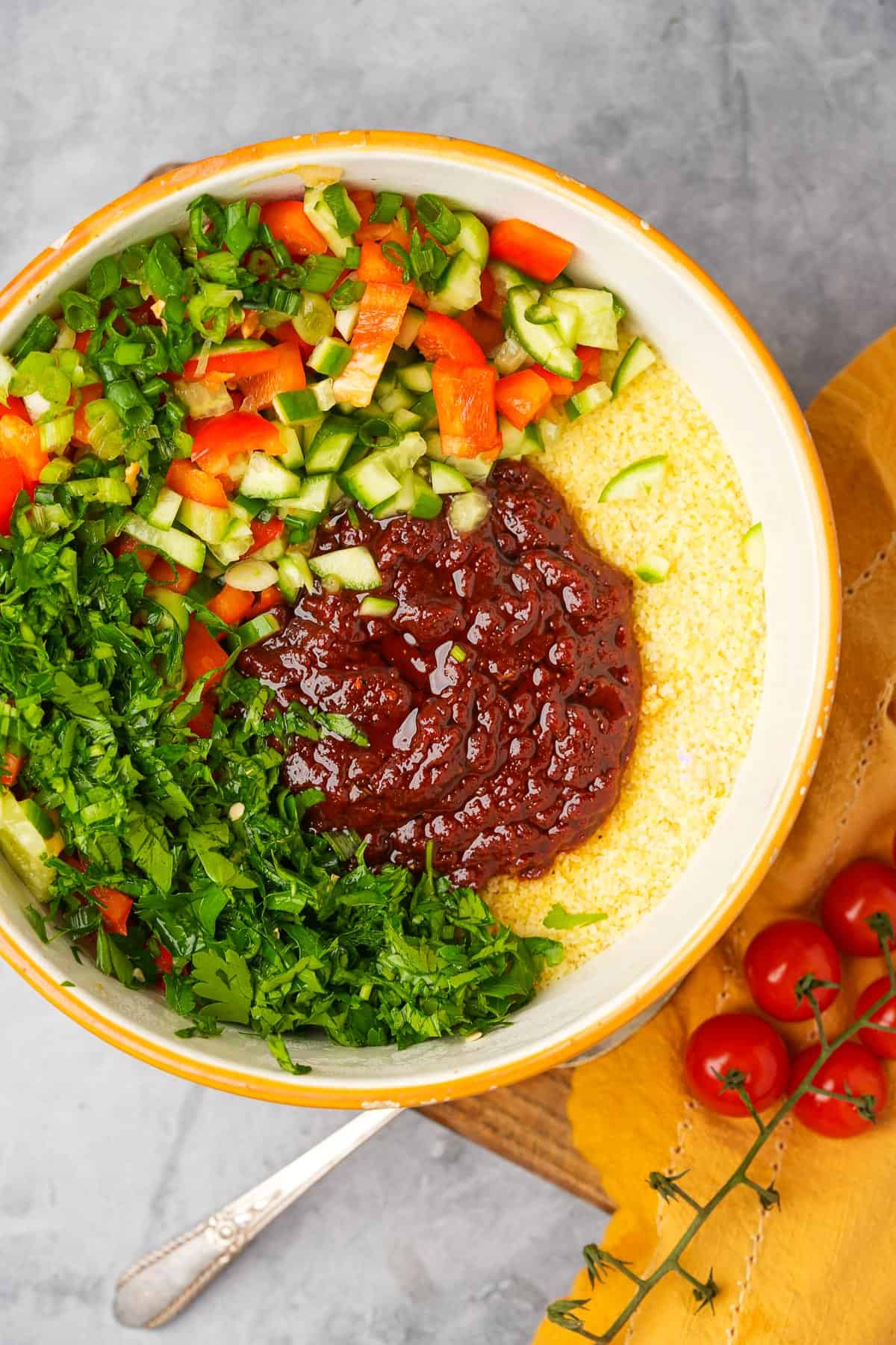 A bowl of hydrated bulgur with vegetables, dressing, and a spoon.