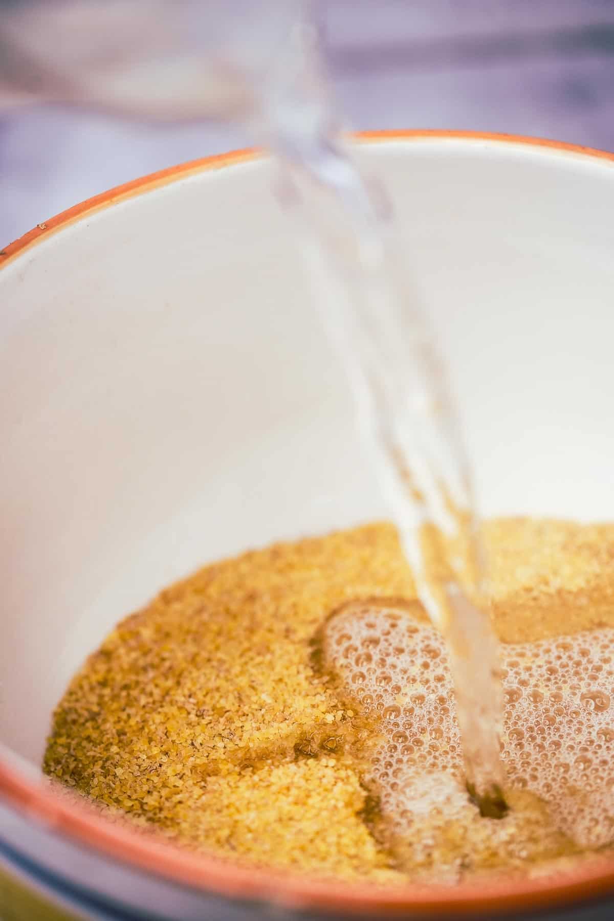 A bowl of boiling water being poured into a bowl of bulgur.