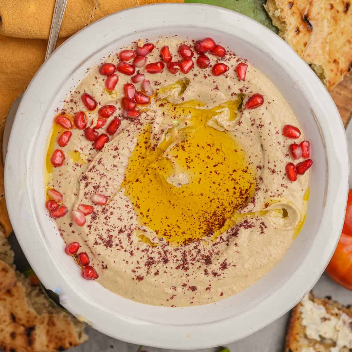 A bowl of mutabal with olive oil and pomegranate seeds.