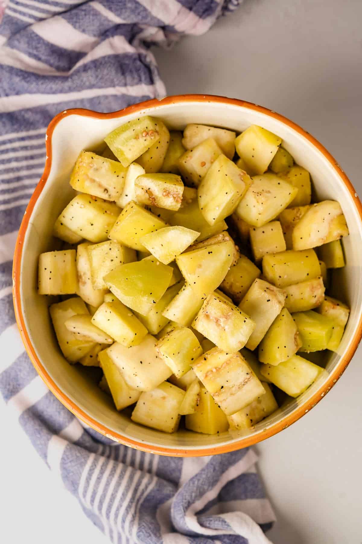 A bowl full of seasoned cubed eggplant in a blue and white striped towel.