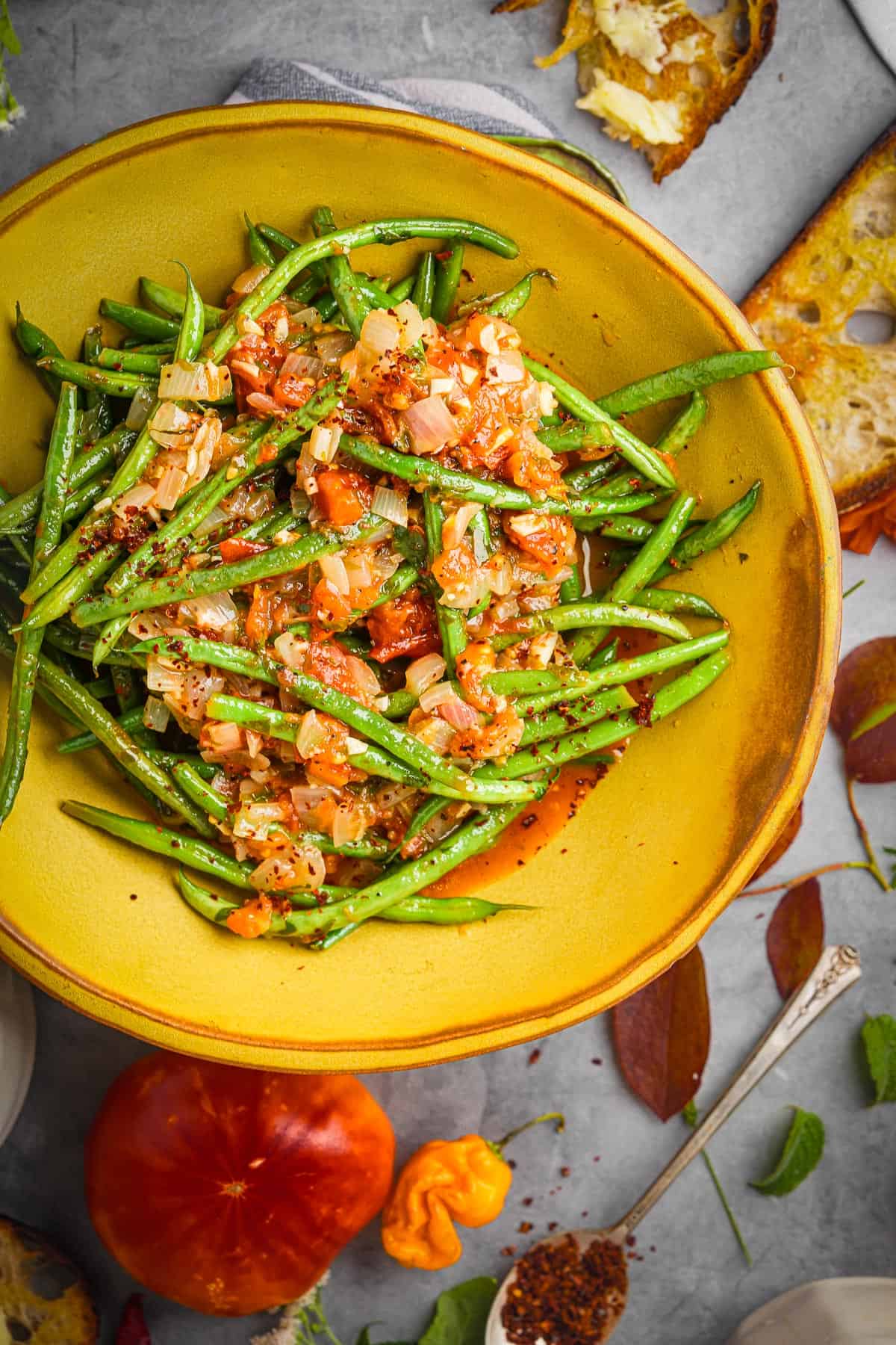 A yellow bowl with Zeytinyağlı Taze Fasulye Tarifi on a table with bread.