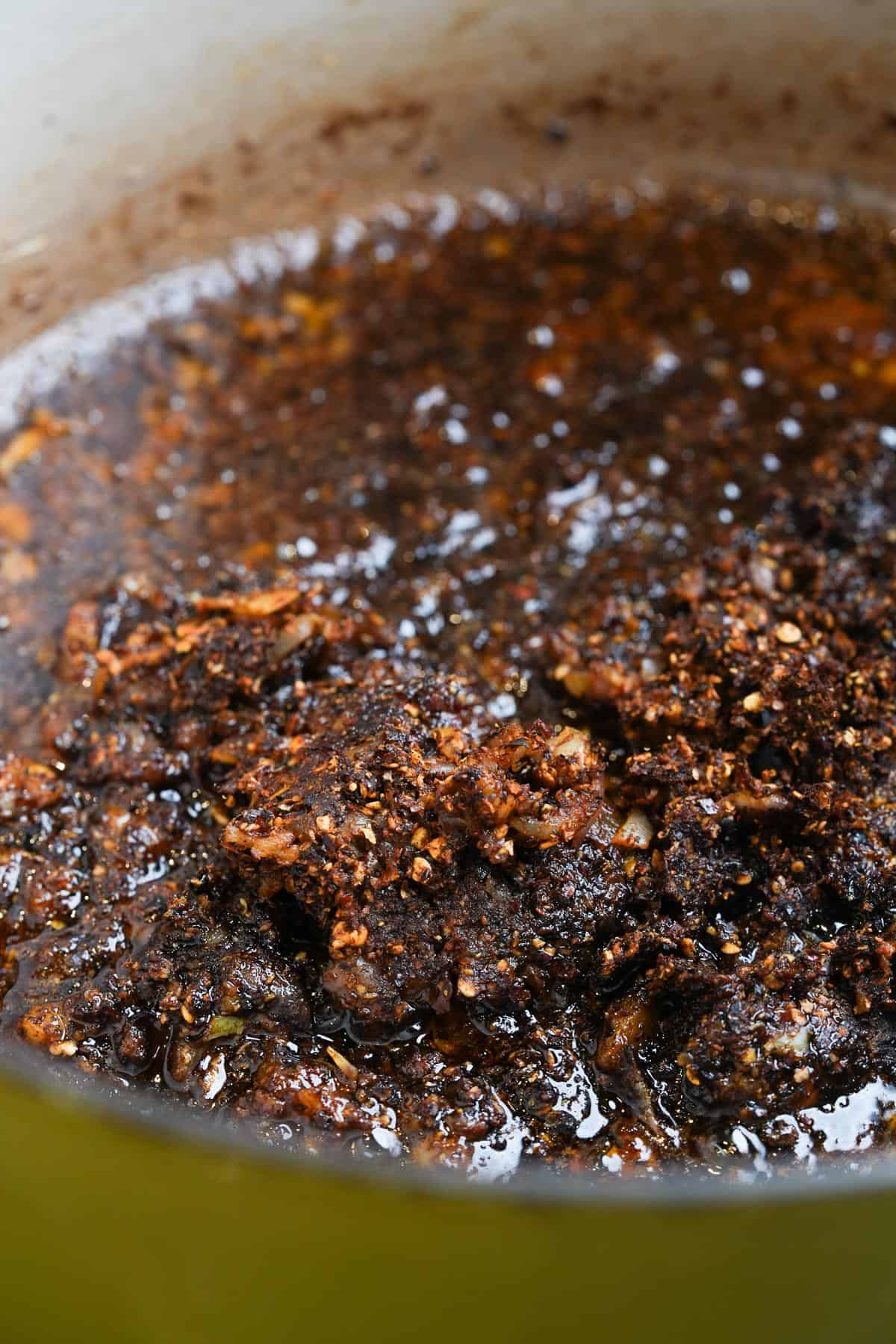 A green pot with a slowly cooking chili sauce in it.
