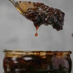 A spoon is pouring nam prik pao into a jar.
