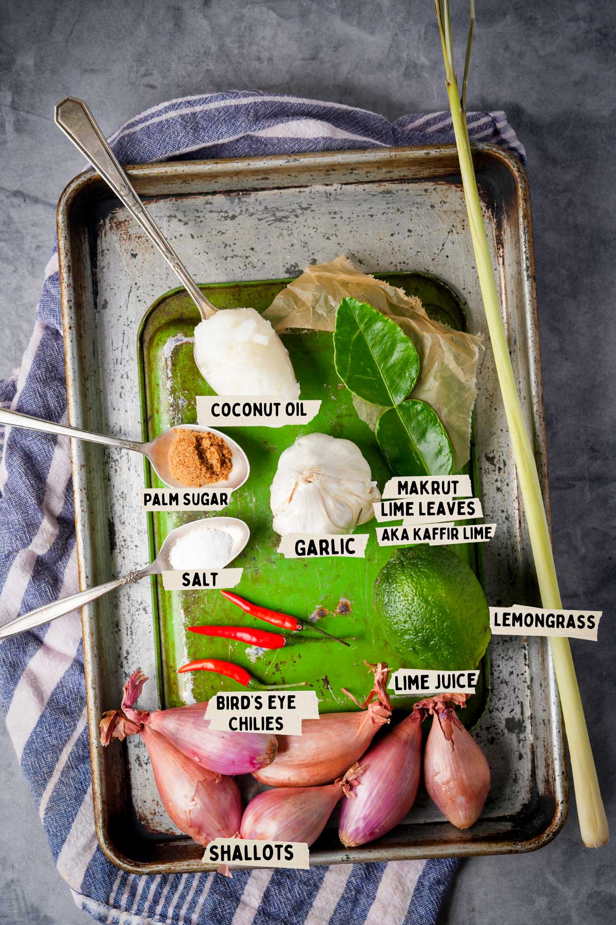 Ingredients for a sambal matah recipe on a tray: coconut oil, palm sugar, salt, garlic, makrut lime leaves, lemongrass, lime, bird's eye chilies, shallots, and lime juice.