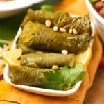 Stuffed grape leaves with lemon and pine nuts in a white dish.