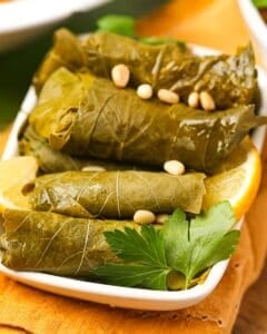 Stuffed grape leaves with lemon and pine nuts in a white dish.
