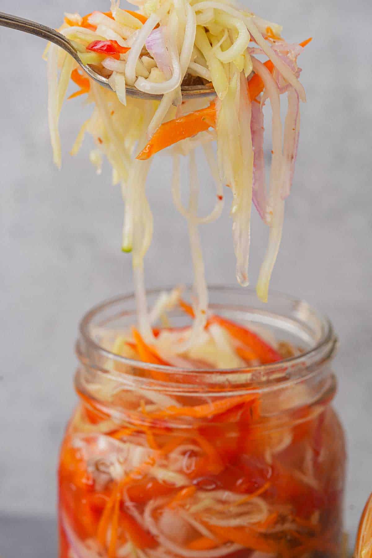 A spoon is being held over a jar of pickled green papaya achara.