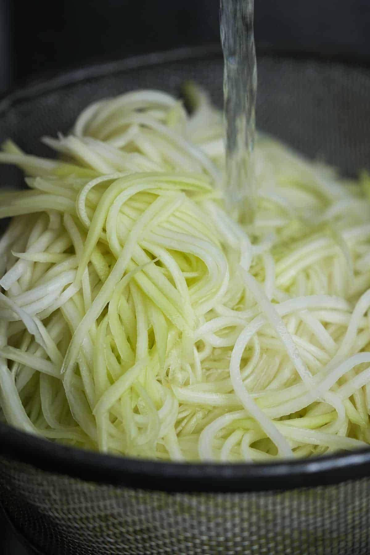 Julienne cut green papaya shreds are being rinsed in a strainer.