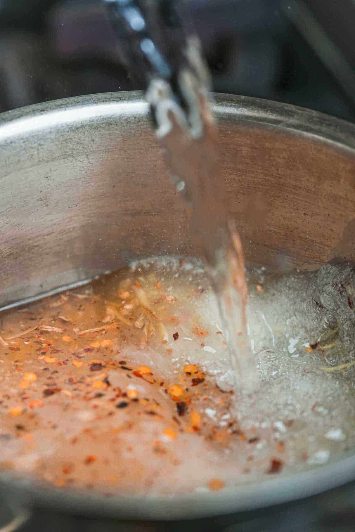 Vinegar being pored into a saucepan of boiling brine ingredients.