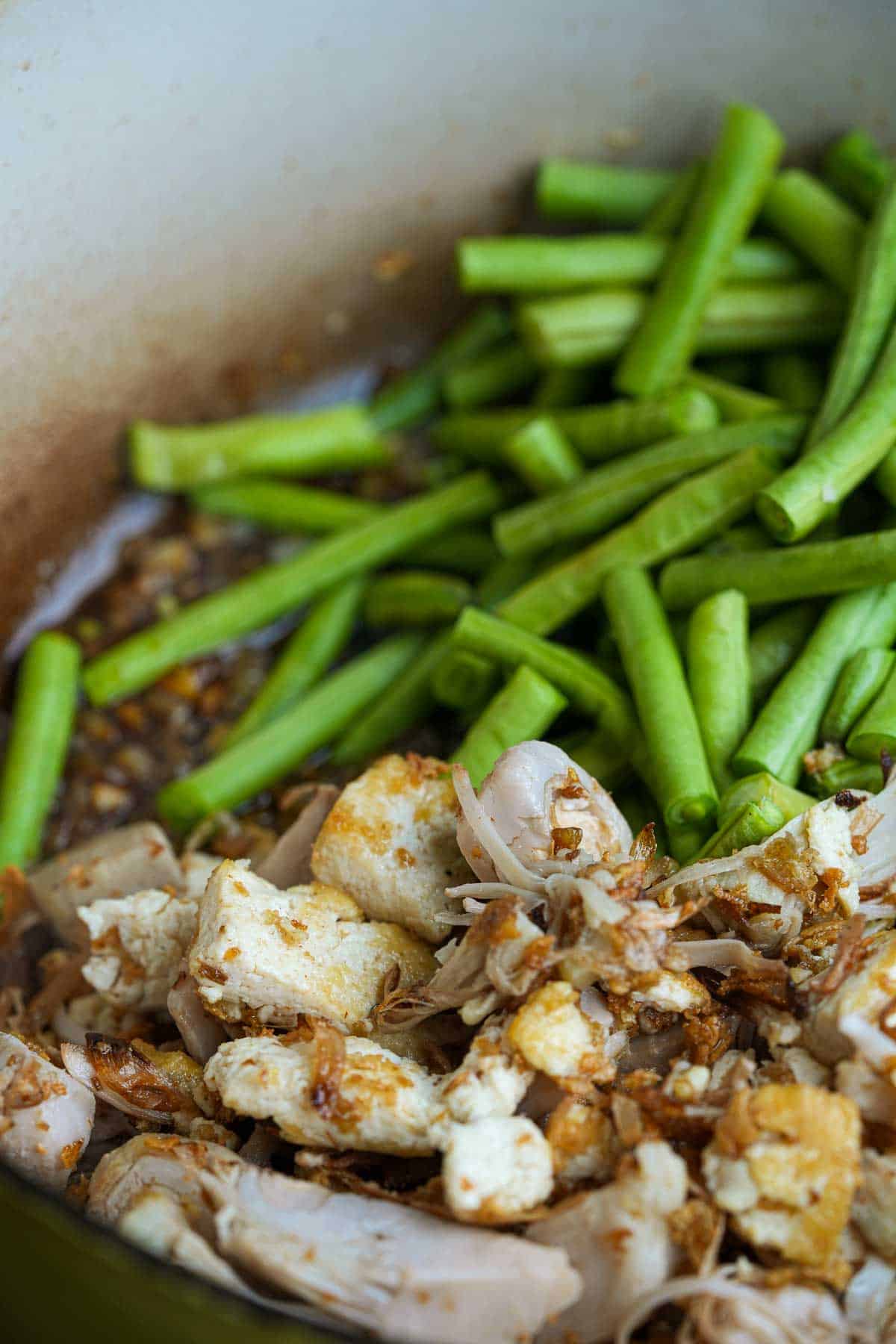 Jackfruit, tofu and cut sitaw are added to the cooking onions, garlic and sauce in a pot.