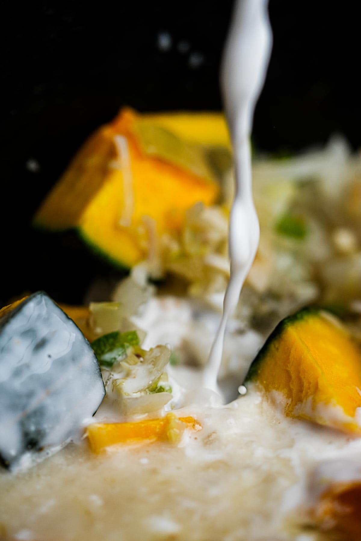 Coconut milk is being poured into a pot with kabocha and aromatics in it.