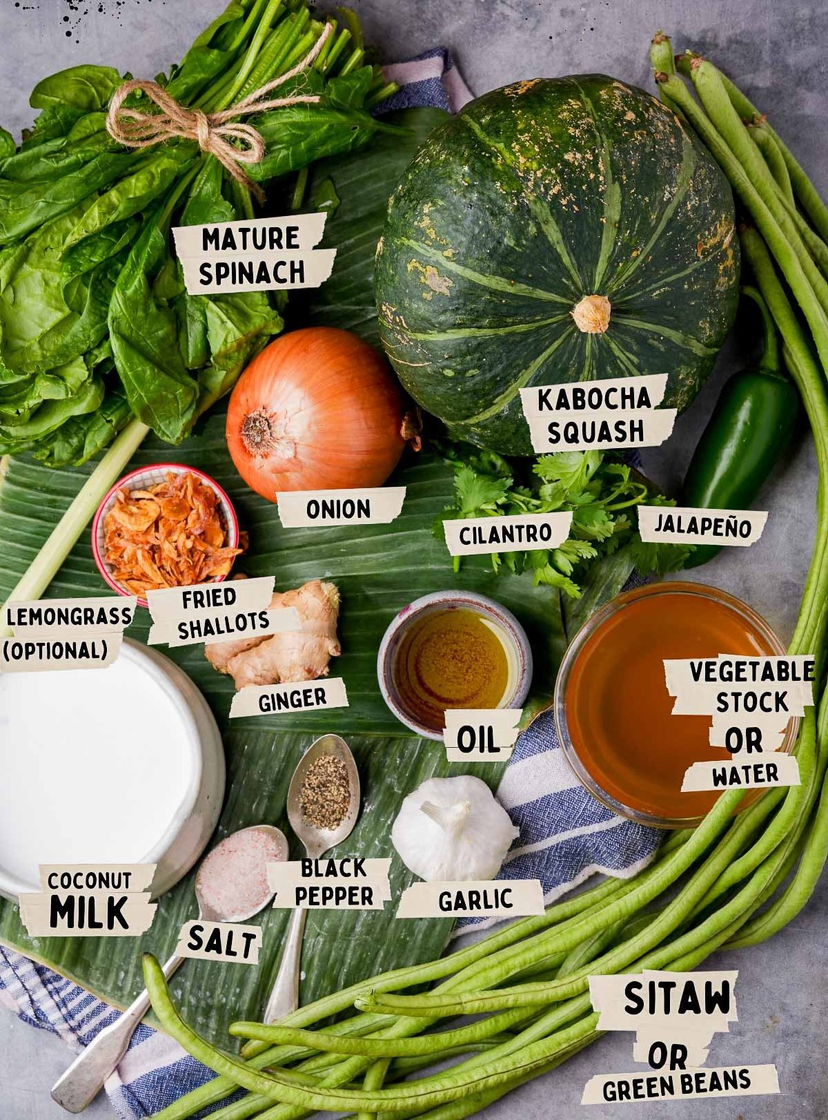 Ingredients for this Ginataang Kalabasa recipe are beautifully displayed on leaves: spinach, kabocha squash, onion, cilantro, jalapeño, lemongrass, fried shallots, ginger, vegetable stock, oil, coconut milk, salt, pepper, garlic, and green beans.