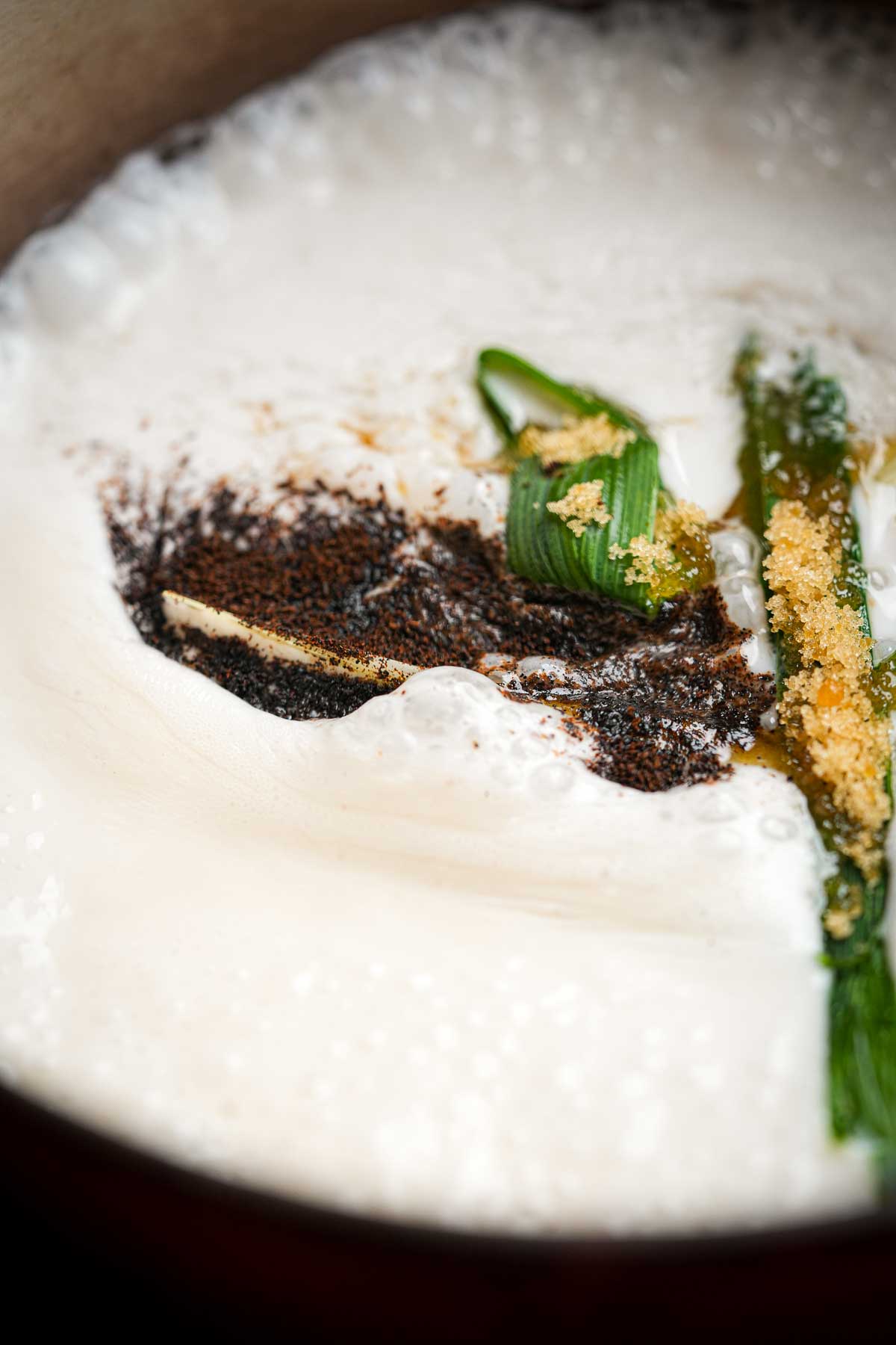 A bowl of coconut cream cooking with vanilla powder, palm sugar and pandan leaves.