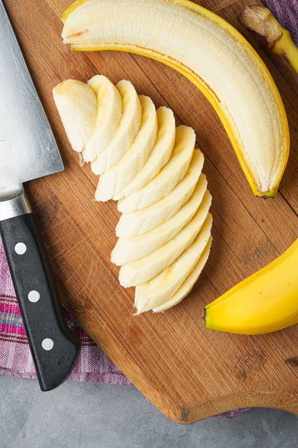 Sliced bananas and a knife on a cutting board.