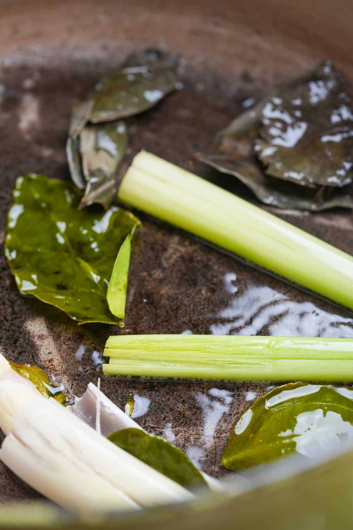 A pot with lemongrass, Indonesian bay leaves, and makrut lime leaves frying in it.