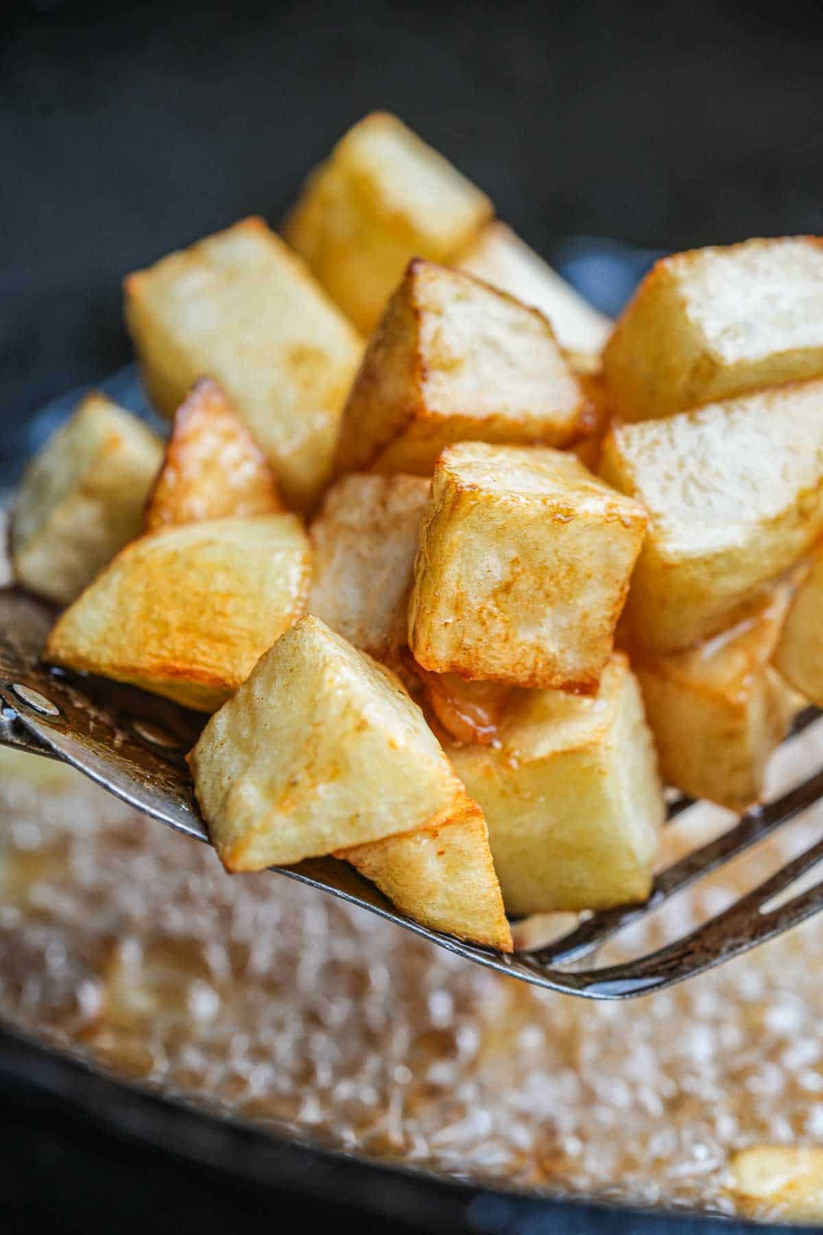 A slotted spoon is used to remove fried potato pieces from pan of hot oil