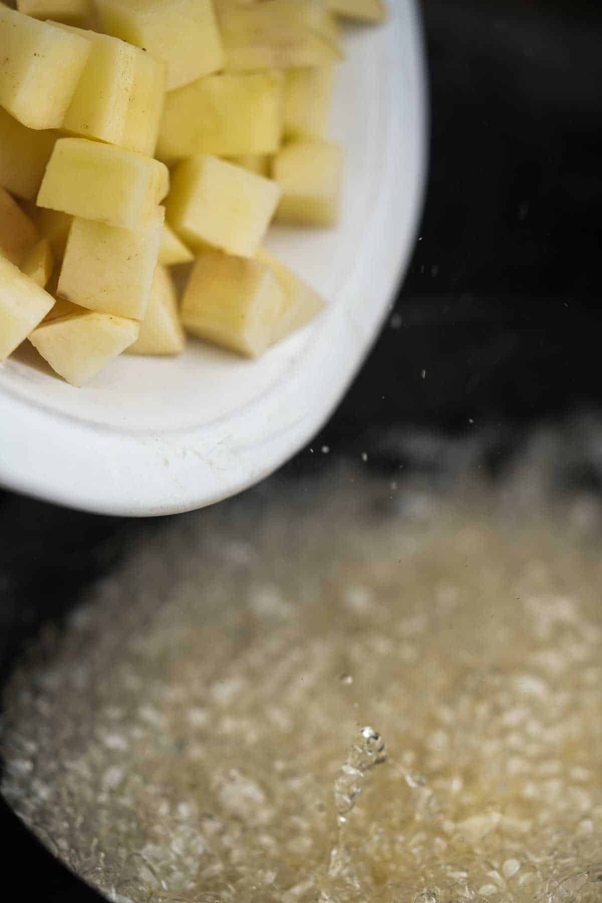 Cubes of potatoes being poured into a pot of hot oil.