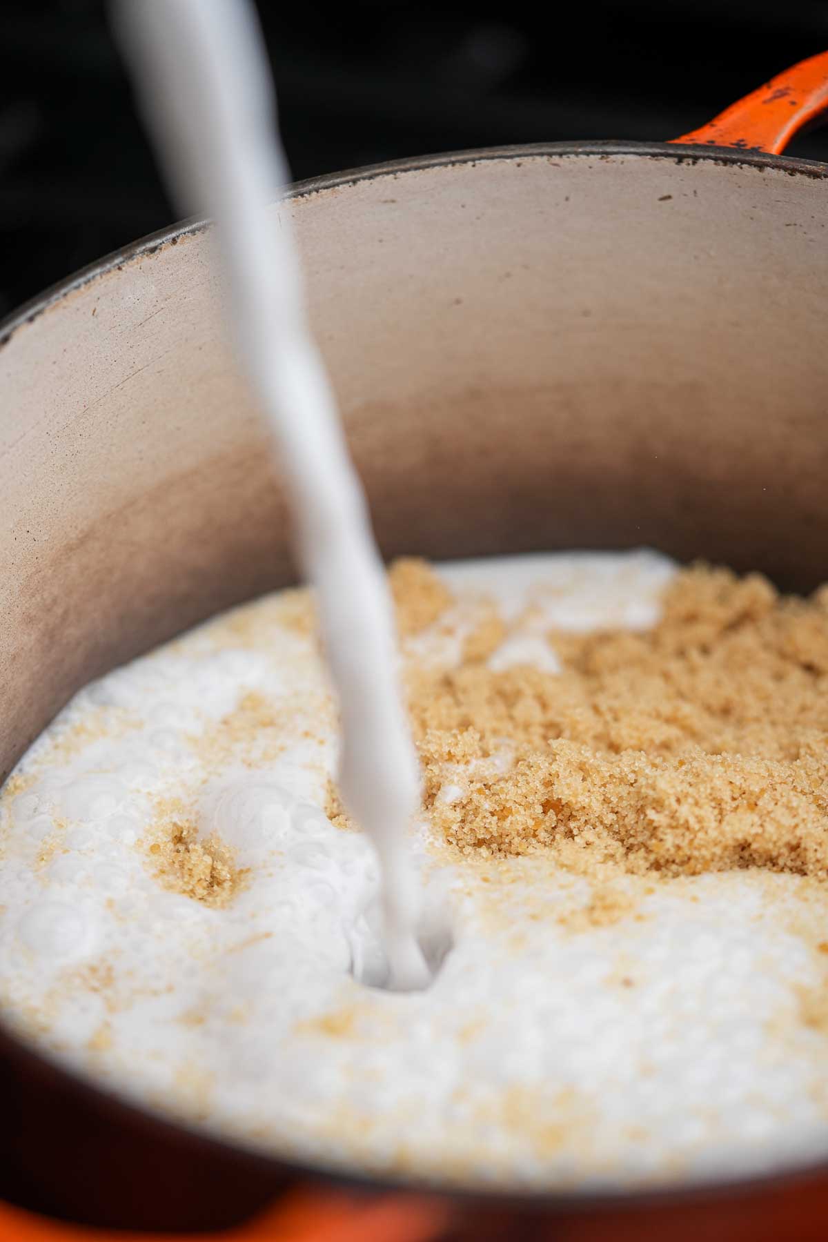 Coconut milk is poured into a pot willed with palm sugar a stove.