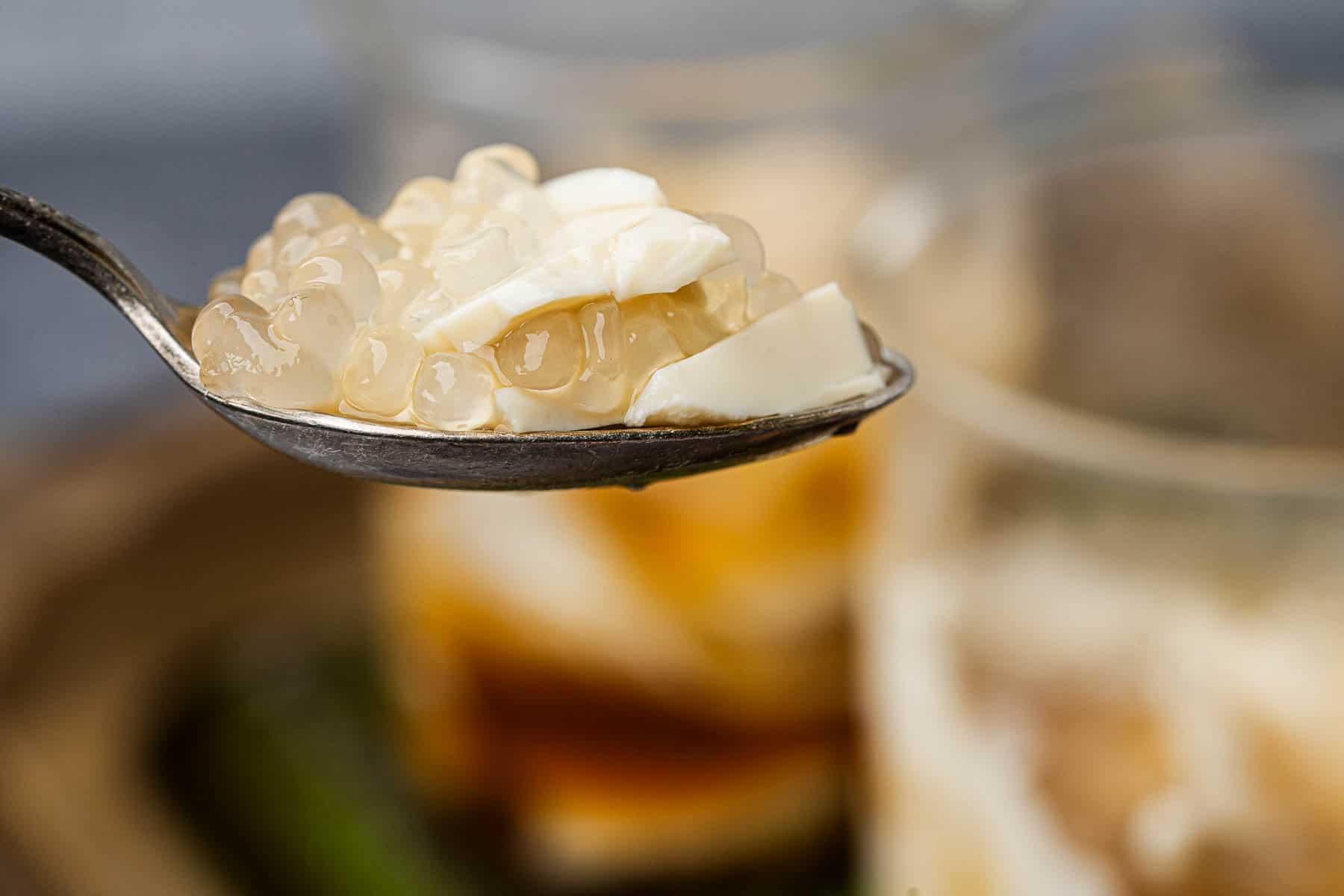 A spoonful of taho held up above a glass full of it.