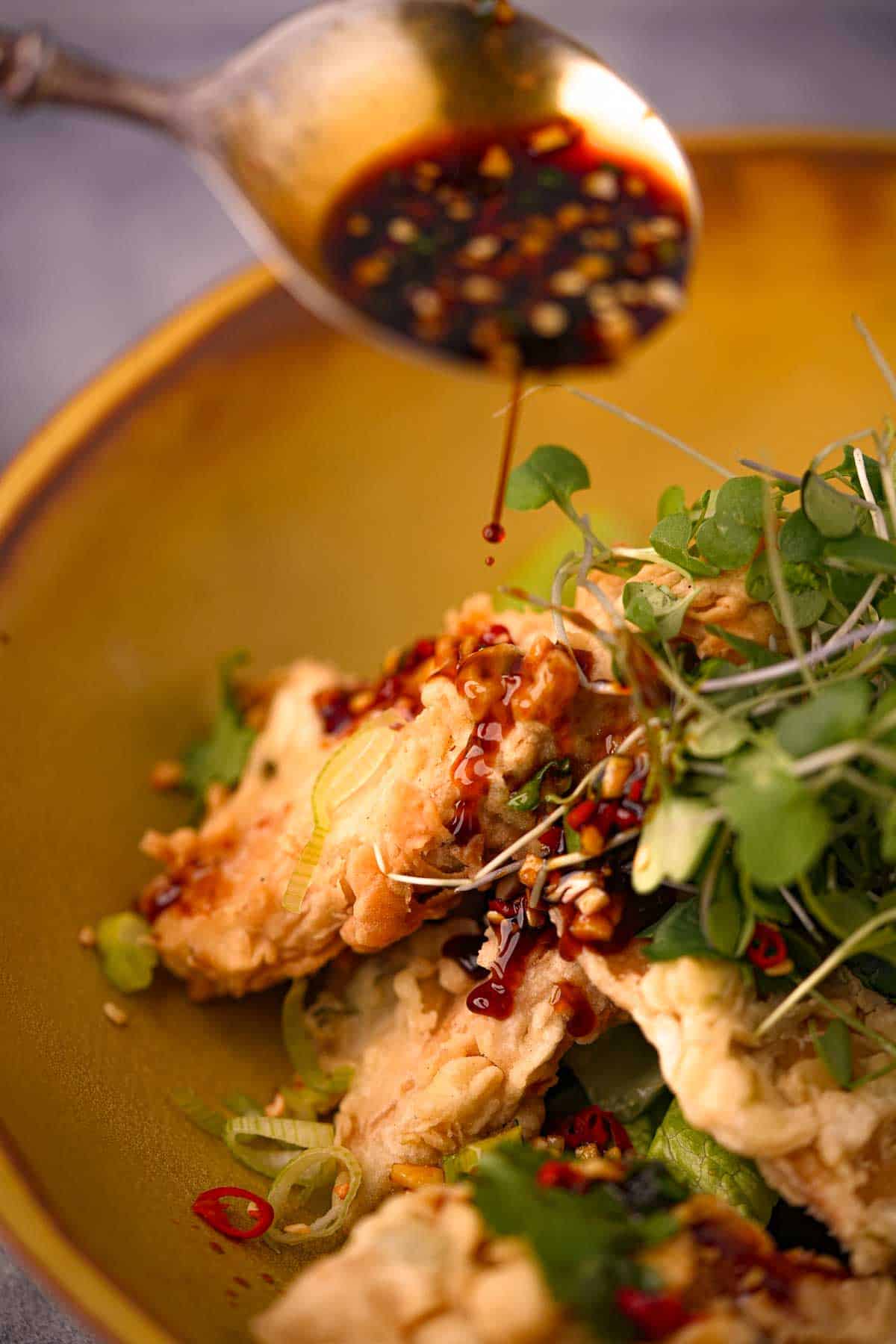 A plate of tempeh mendoan with a sauce being poured over it.