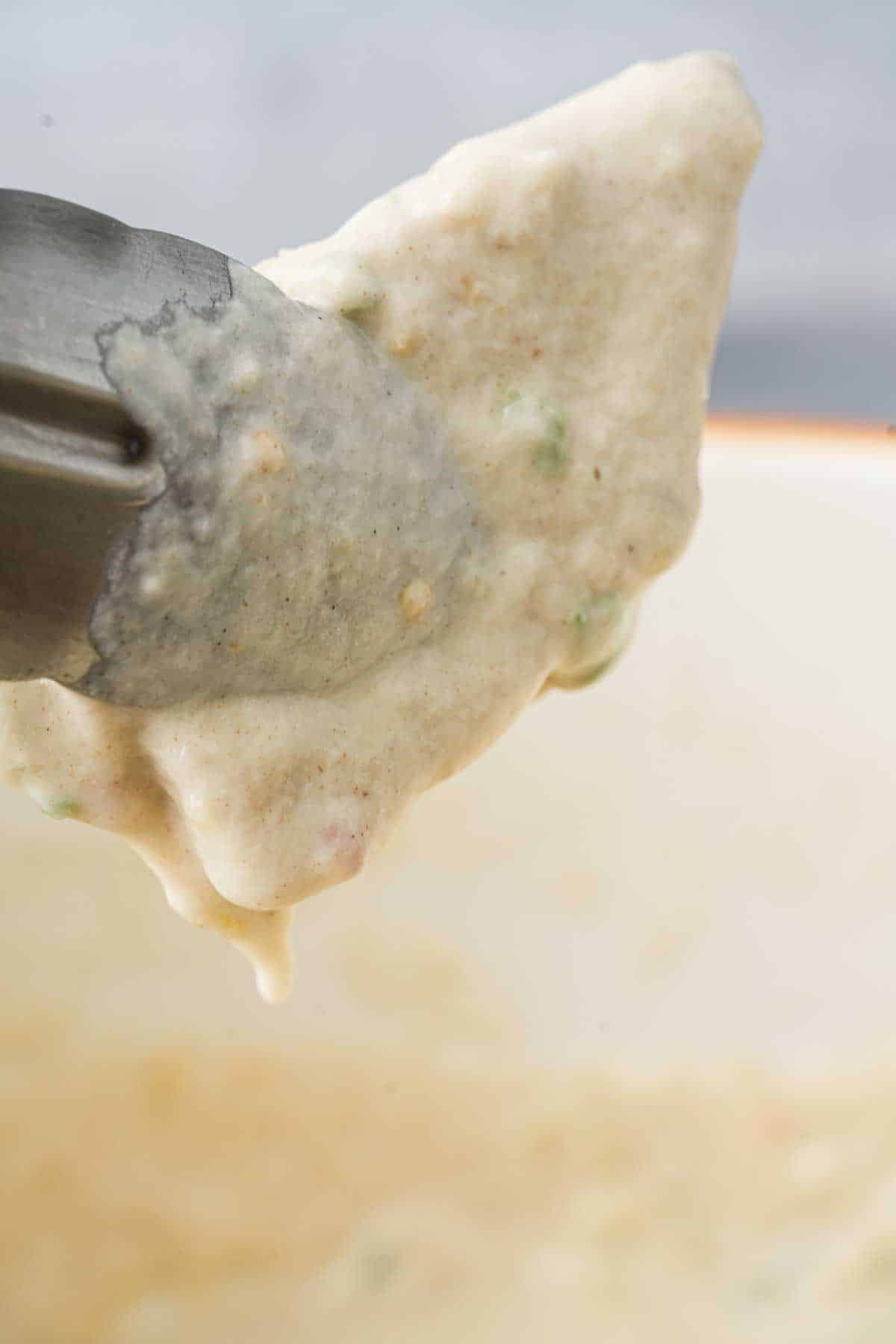 Tongs being used to dip a piece of tempeh in batter.