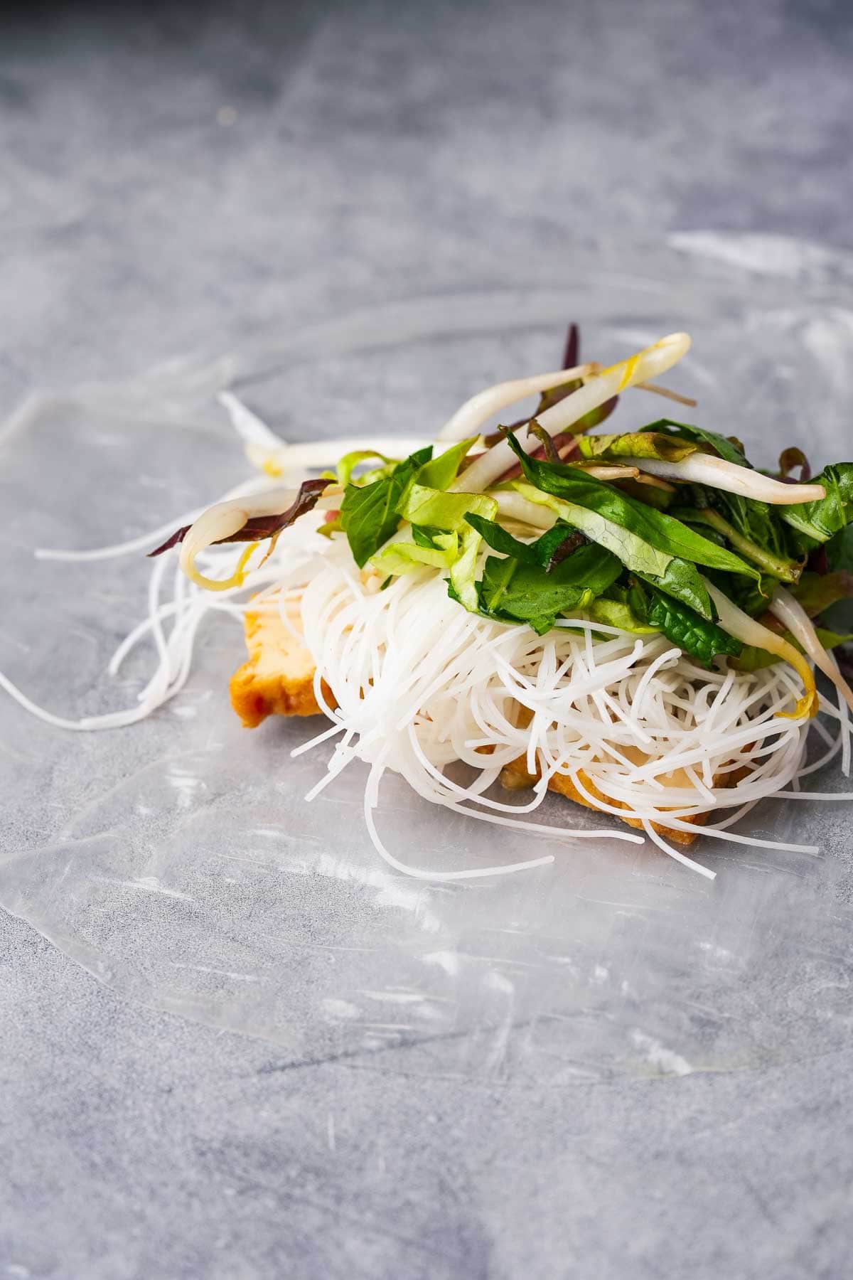 A piece of soaked rice paper with noodles, tofu and greens on it.