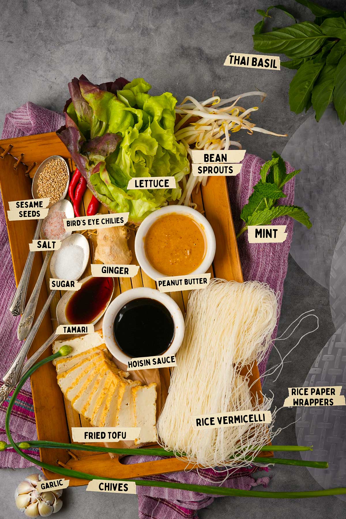 Ingredients for Banh Trang Cuon, or Vietnamese spring rolls, on a tray: lettuce, bean sprouts, mint, Thai basil, rice vermicelli, rice paper wrappers, fried tofu, sauces, and spices. This classic dish offers a harmonious blend of fresh flavors and textures.