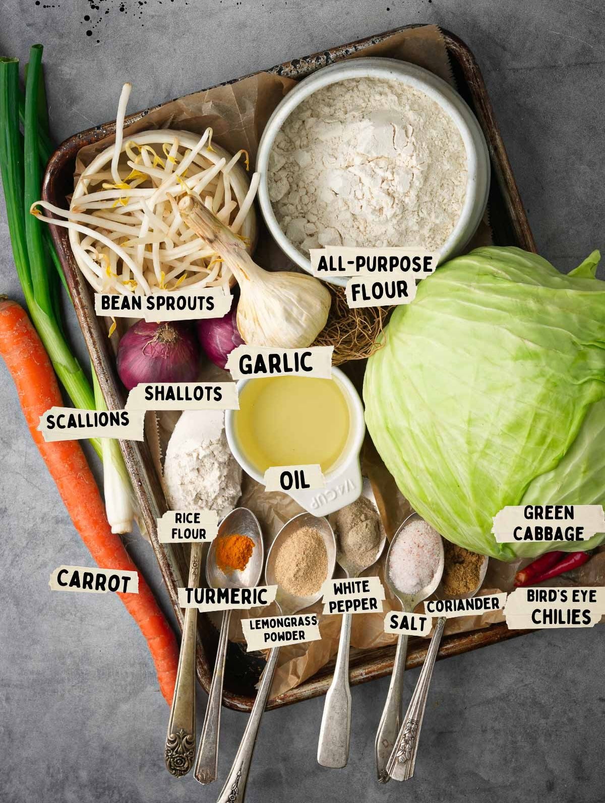 A tray holds cooking ingredients for bakwan sayur, including bean sprouts, all-purpose flour, green cabbage, garlic, oil, shallots, scallions, carrot, rice flour, turmeric, lemongrass powder, white pepper, salt, coriander and bird's eye chilies.