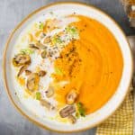 A bowl of carrot lentil soup garnished with coconut milk, chili oil and sliced chestnuts.