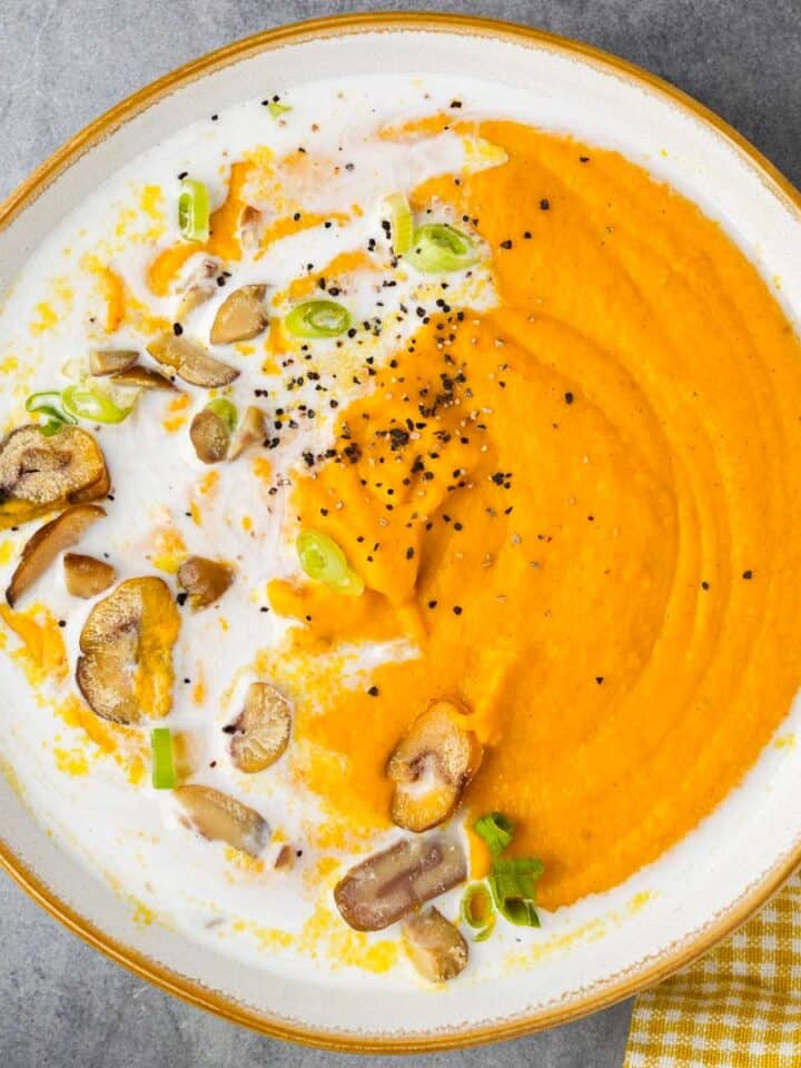 A bowl of carrot lentil soup garnished with coconut milk, chili oil and sliced chestnuts.
