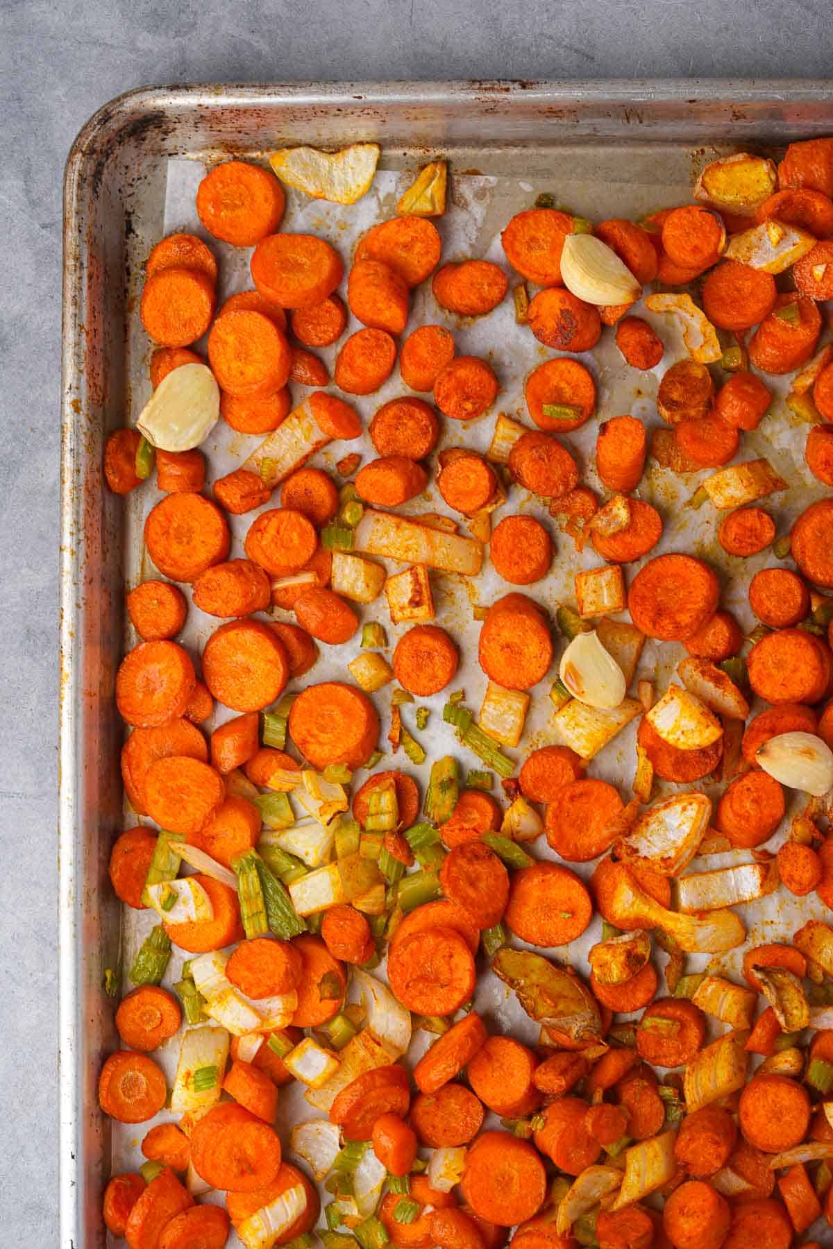 Roasted celery, garlic, ginger, carrots and onions on a baking sheet.