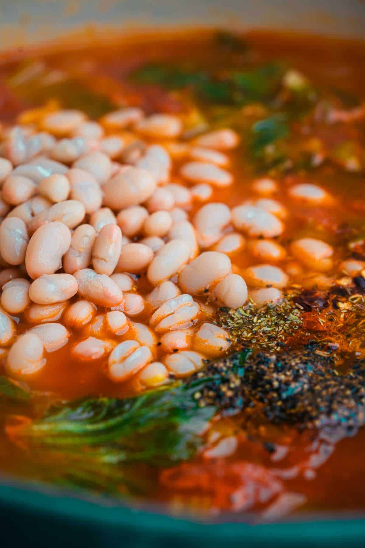 White beans and seasonings are added to a pot of soup.