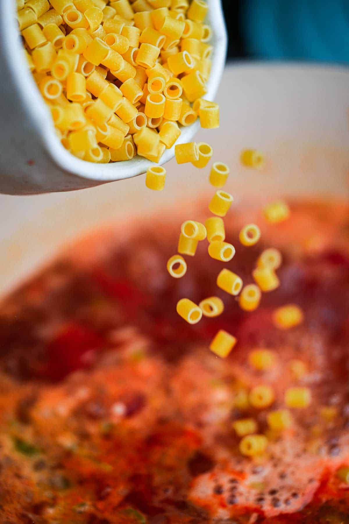 A bowl of pasta being poured into a pot of soup.